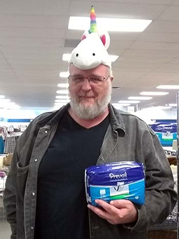 The author wearing a whit and rainbow unicorn hat and holding a pack of Prevail Male Guards at a Goodwill store