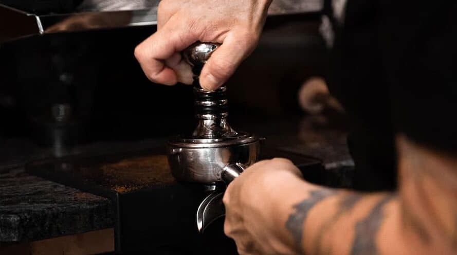 Person tamping ground coffee in portafilter 