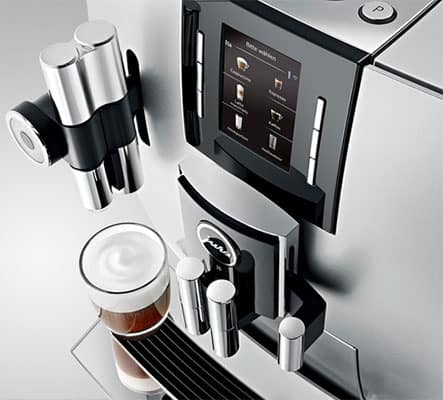 The Jura 15150 J6 Coffee Machine and a glass filled with specialty coffee under its milk spout