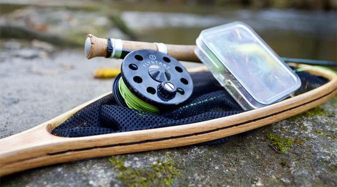 fly fishing reel, lures, and net on a huge slab of stone with moss