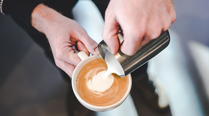 barista pouring steamed milk in coffee and making latte art