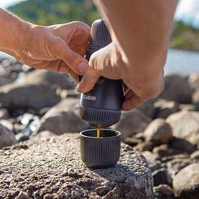 Man pulling a shot with two hands from the Nanopresso placed over a big rock in front of the lake and mountain