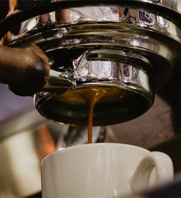espresso dripping out the bottomless portafilter into a white ceramic espresso cup