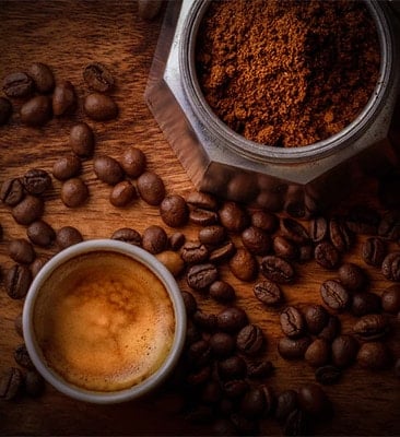 whole coffee beans, ground coffee beans, and a shot of espresso on a wooden table
