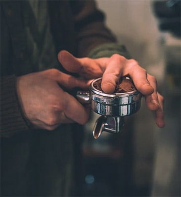 barista using his finger to remove excess grinds from the portafilter