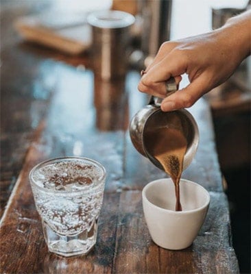 person pouring coffee in a cup beside a glass of water