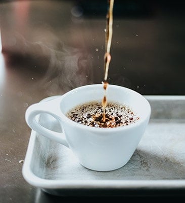 a white cup of steaming espresso on a tray