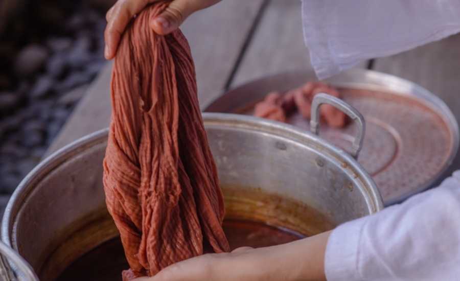 A person in a white long-sleeved shirt dyeing a cloth inside a stock pot