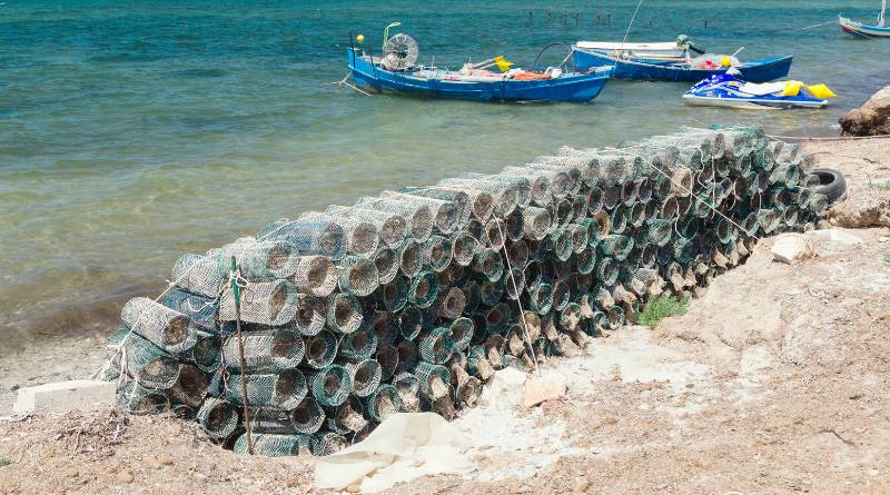 Fish trap baskets on the shore and three small boats and a jet ski on the beach